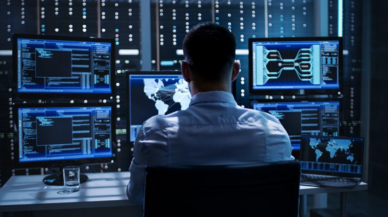 System Security Specialist Working at System Control Center. Roo System Security Specialist Working at System Control Center. Room is Full of Screens Displaying Various Information.